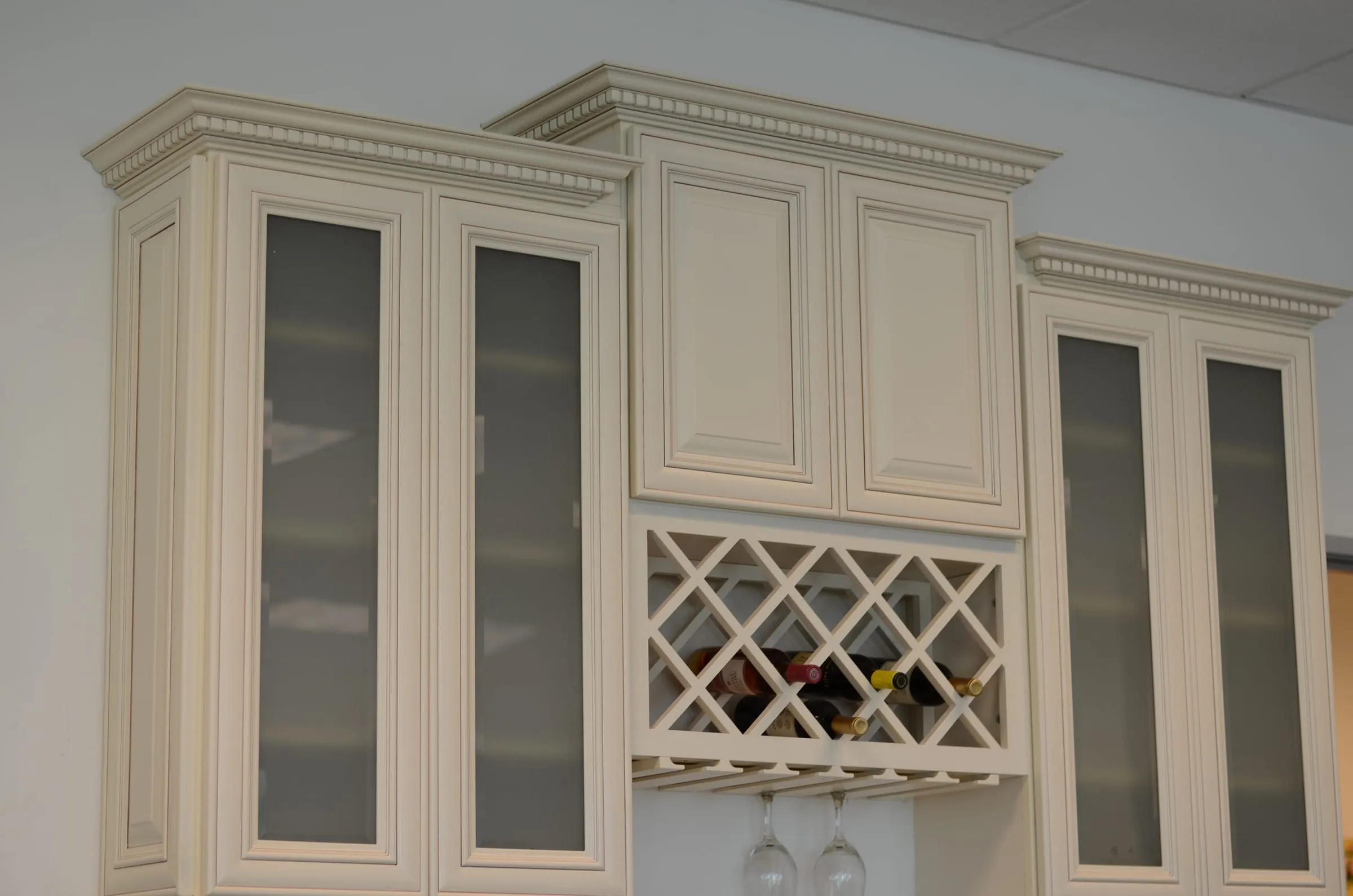 Antique White uppers with crown molding, frosted-glass doors, and a built-in wine lattice