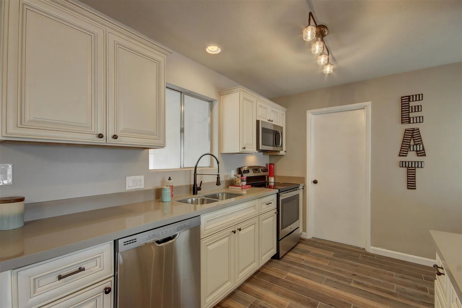 Antique White cabinet run with gray counters, stainless dishwasher, and a wood-look floor