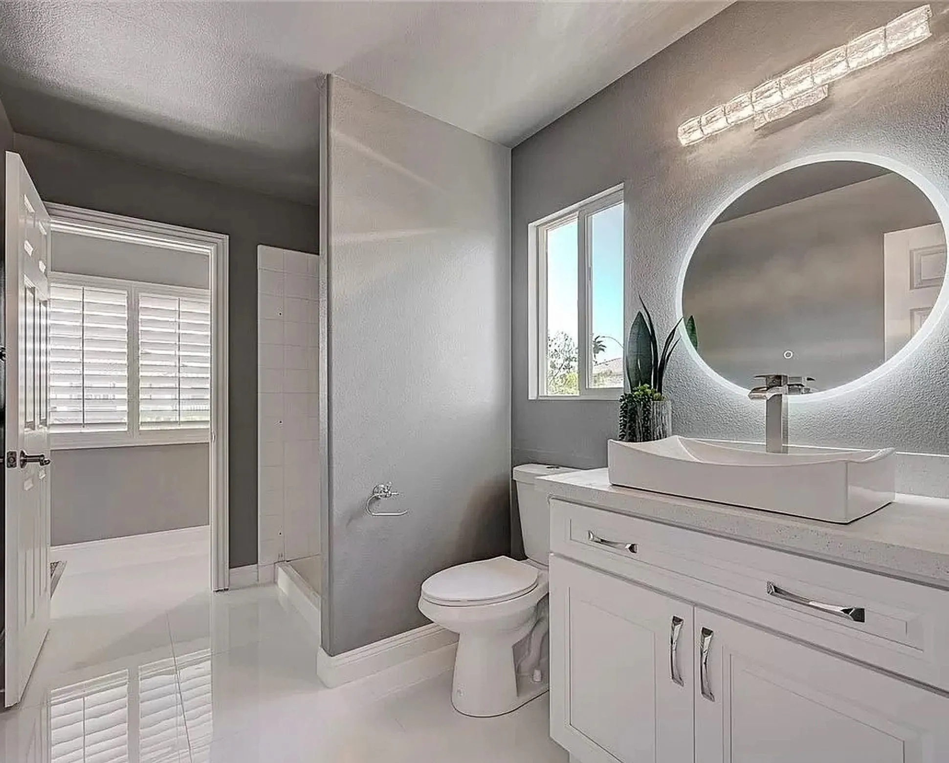 White bath with a round lit mirror, a white vanity, and a grey accent wall