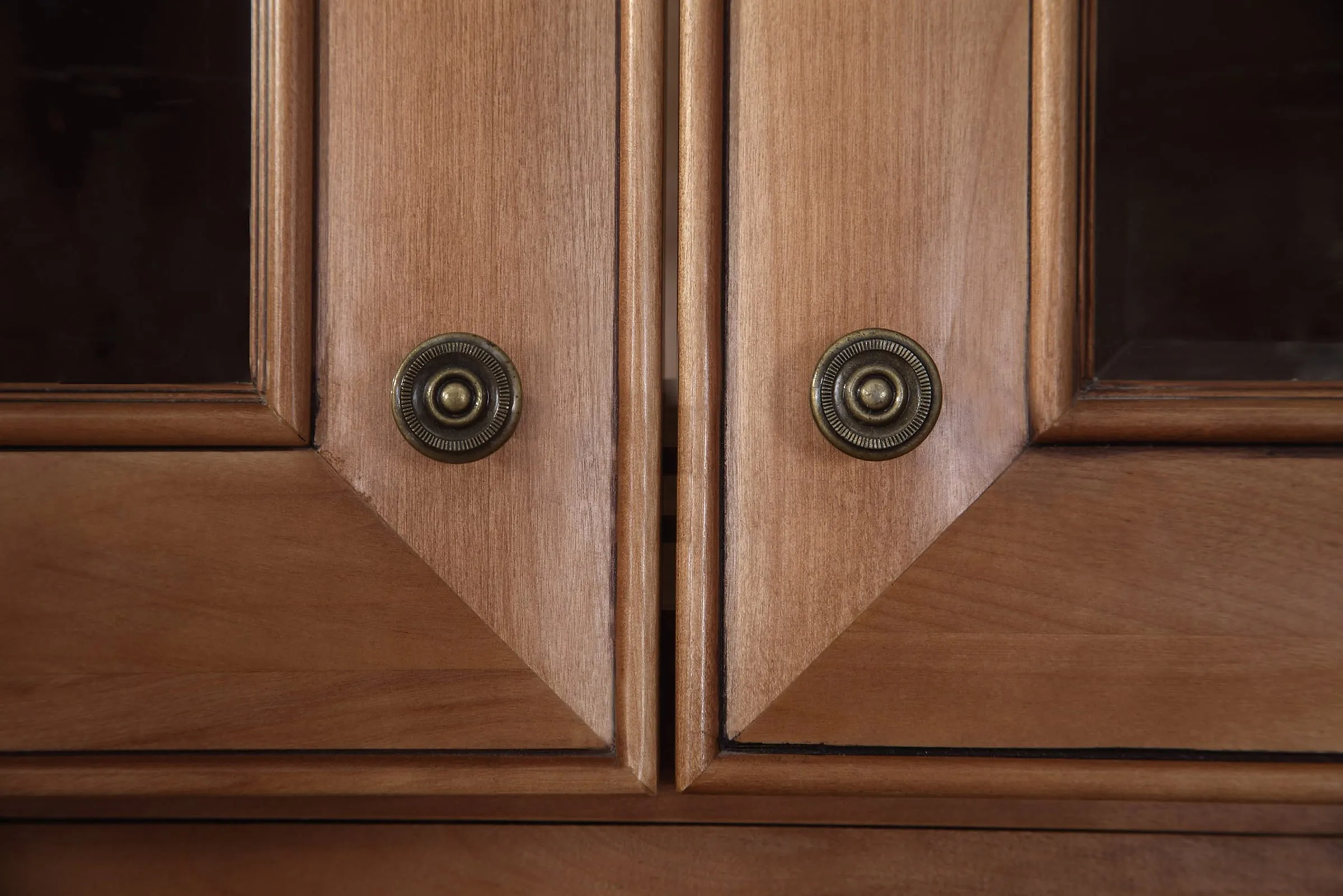 Close-up of ginger-stained mitered cabinet doors with antique-brass round knobs