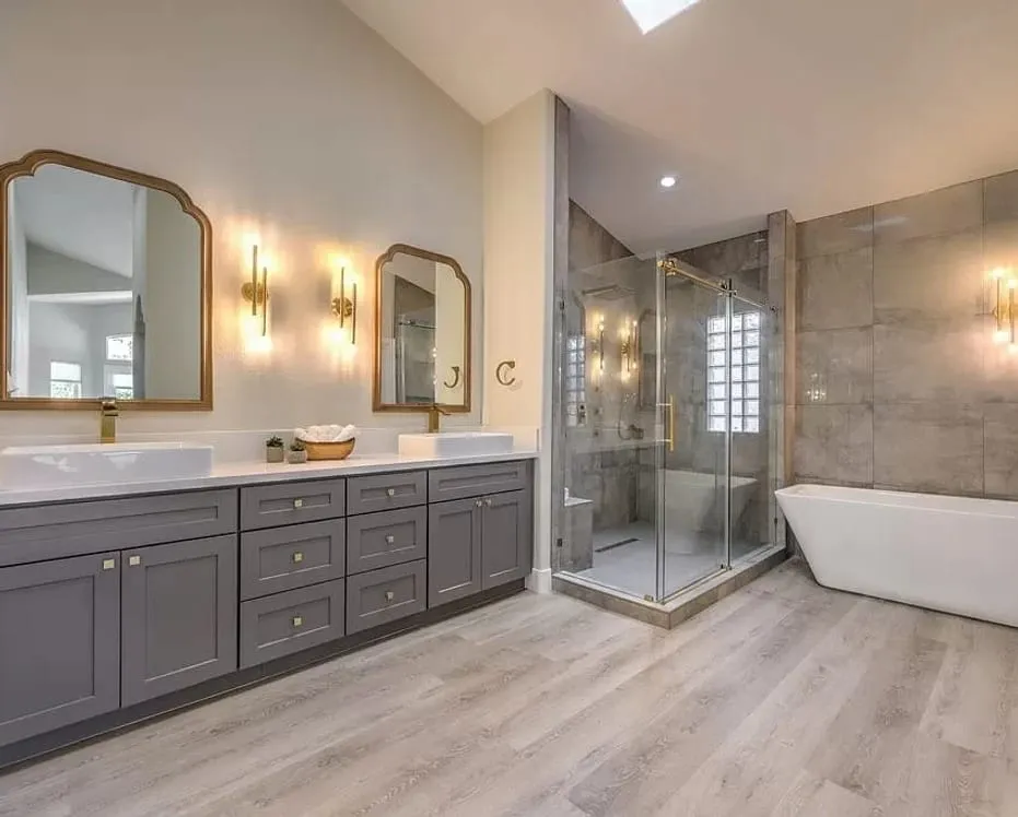 Greige vanity bath with gold-framed mirrors and a glass shower