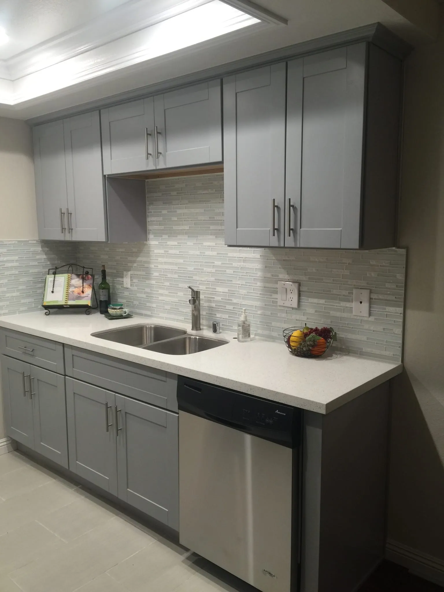 Ash Gray shaker kitchen wall run with a double sink, stainless dishwasher, light quartz counters, and a linear stone backsplash