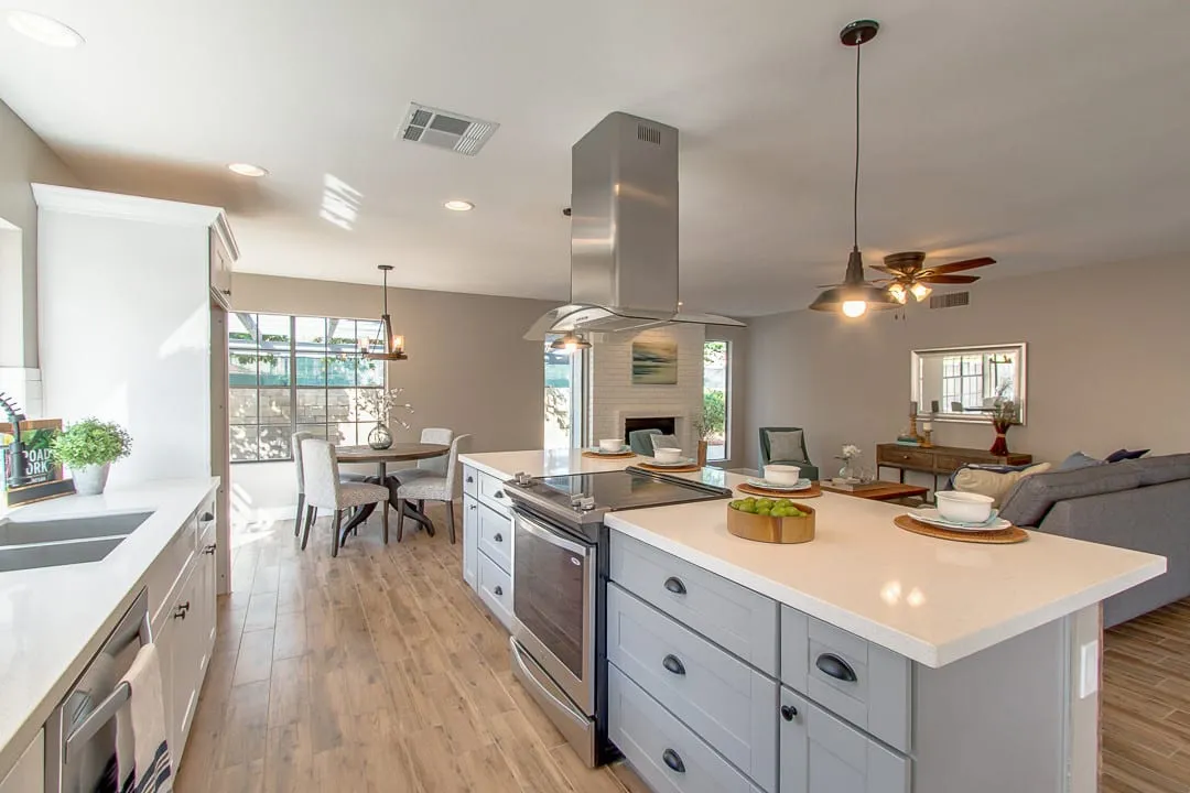 Open-plan kitchen with a pale gray shaker island, stainless range and island hood, and wood-look floors