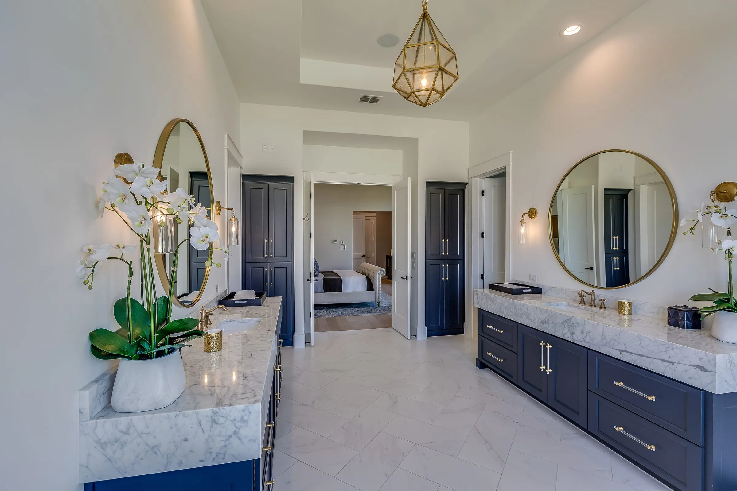 Navy blue shaker double vanity with marble tops, round mirrors, and brass fixtures