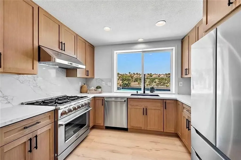 Light oak shaker kitchen with a pro range, marble backsplash, and a window over the sink