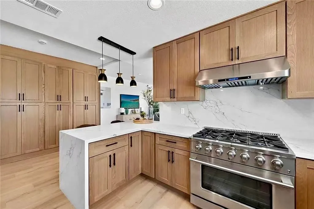Oak shaker kitchen with a peninsula, waterfall marble, and a stainless range