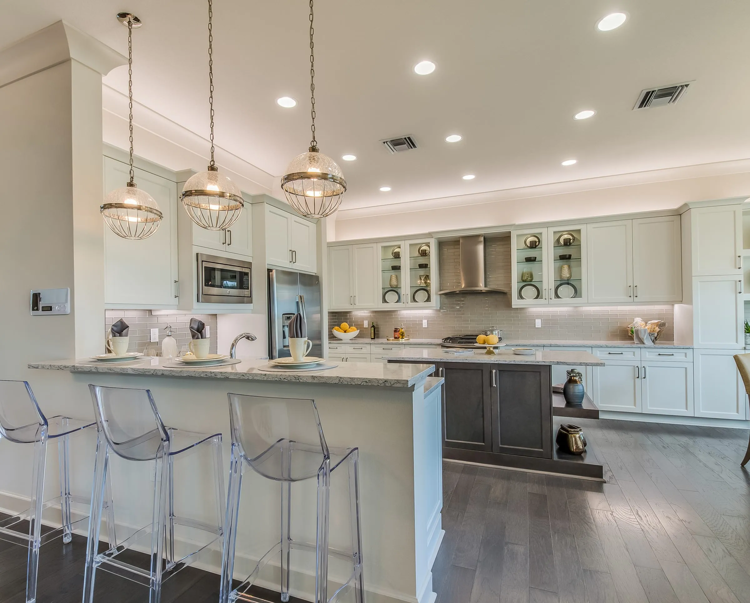 White and cream kitchen with a dark island, clear ghost stools, and globe pendants