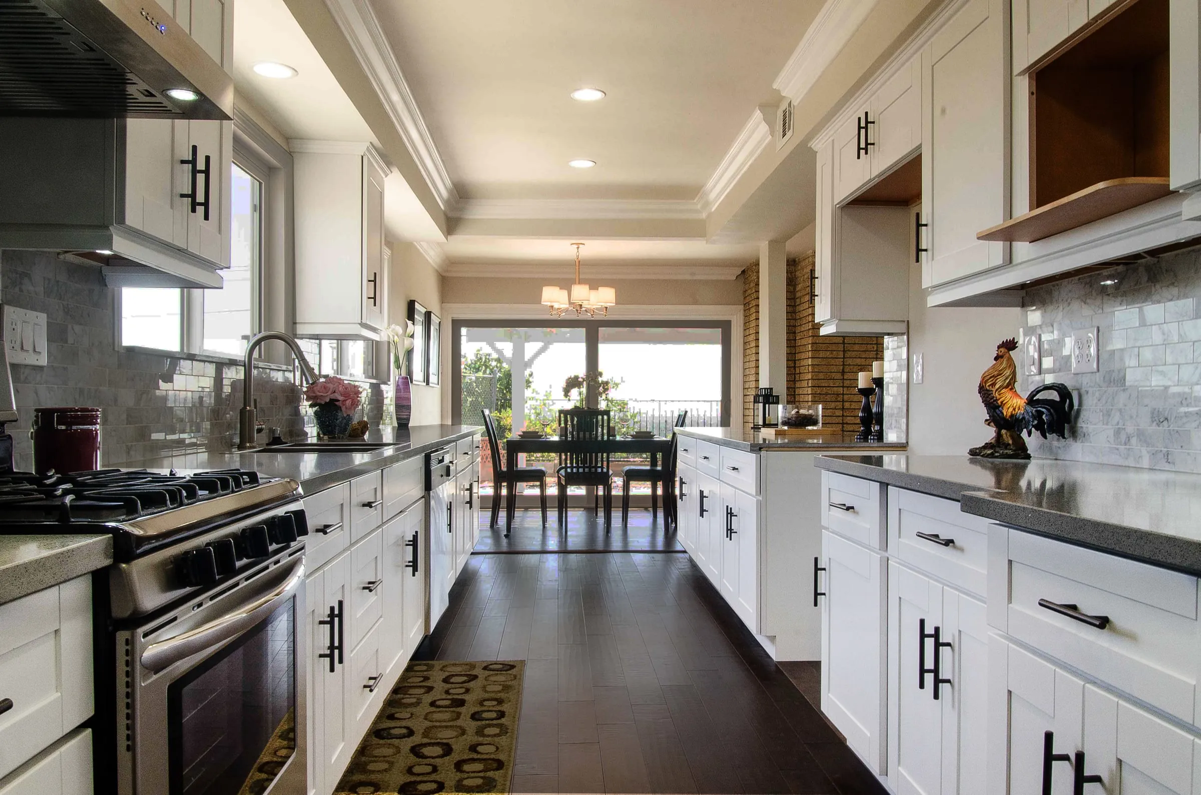 White shaker galley kitchen with dark counters, tile backsplash, and a hardwood floor running to a dining area