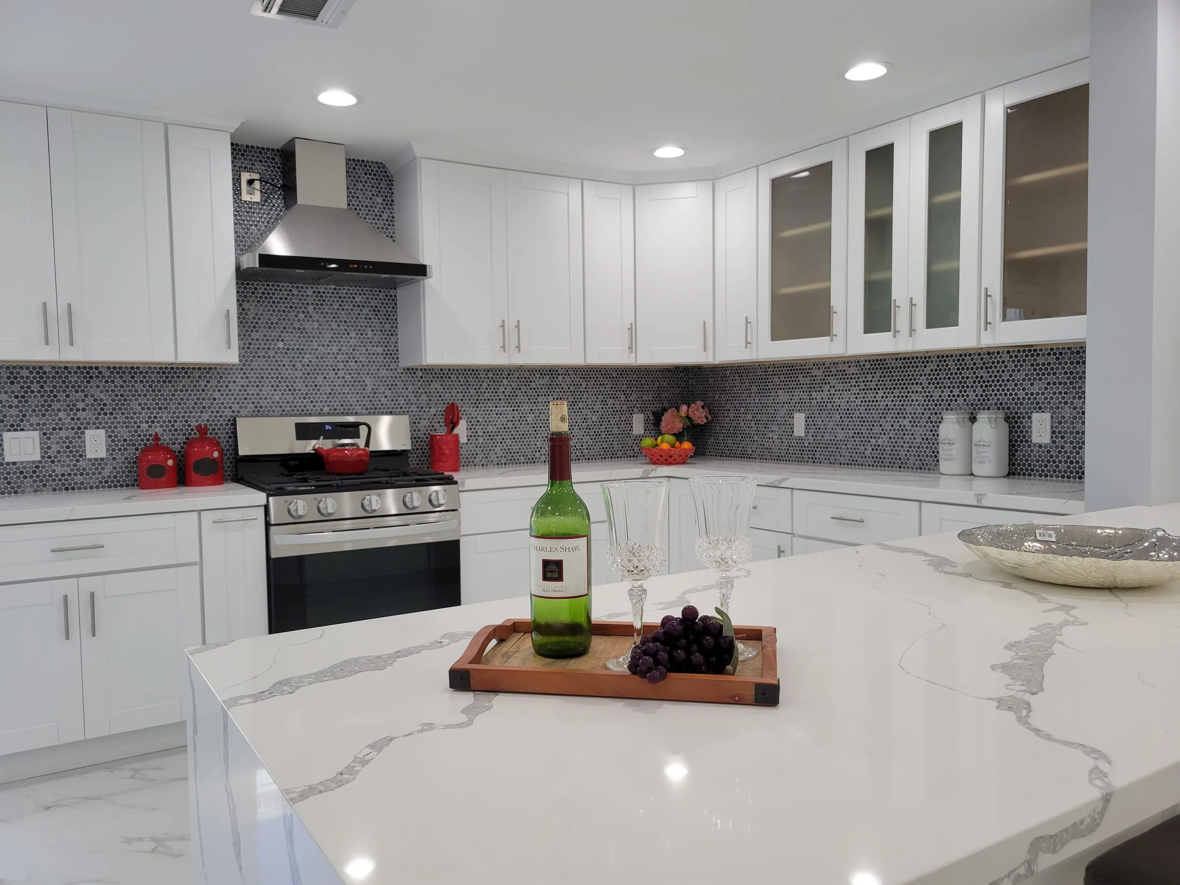 White shaker kitchen with a quartz island, stainless chimney hood, and a gray mosaic backsplash